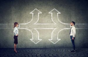 A man and a woman facing each other with chalk-drawn arrows on a concrete wall behind them, representing decision-making and communication challenges during a merger process.