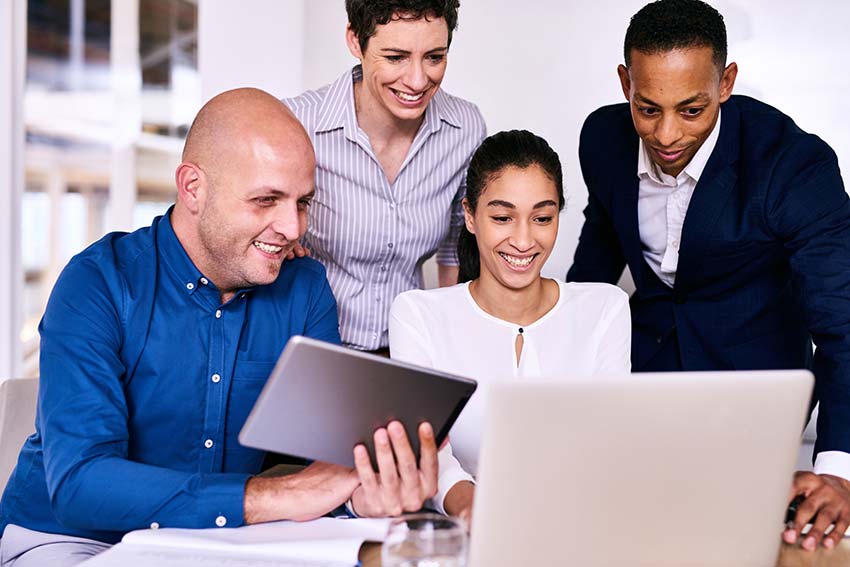 Team of professionals collaborating around a laptop and tablet, representing seamless integration and unified business strategy during a merger.