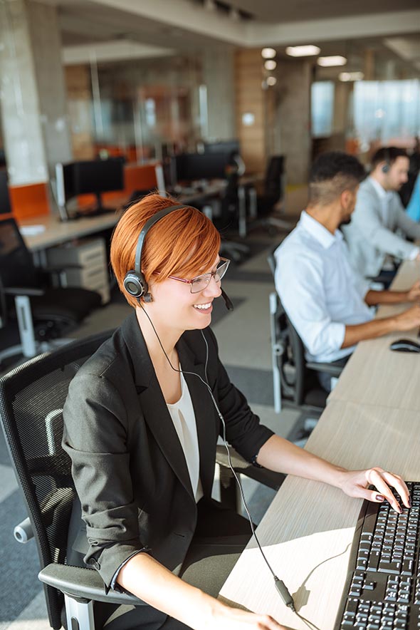 Smiling support center agent with headset assisting clients in a modern office, representing global service integration.
